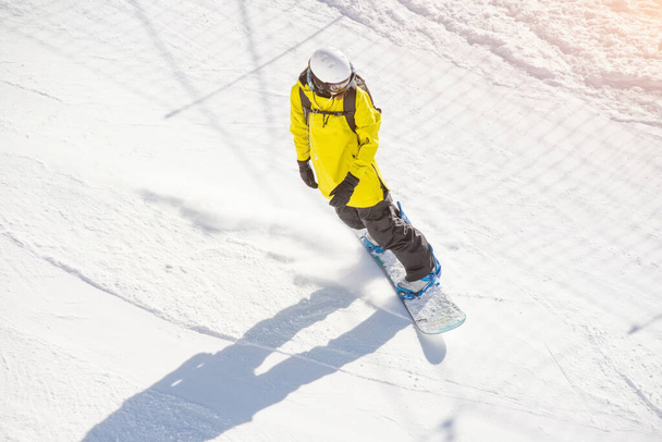 Snowboarder in een helm en met een rugzak op zijn rug rijdt op een zonnige dag over een bergpad - Foto, afbeelding