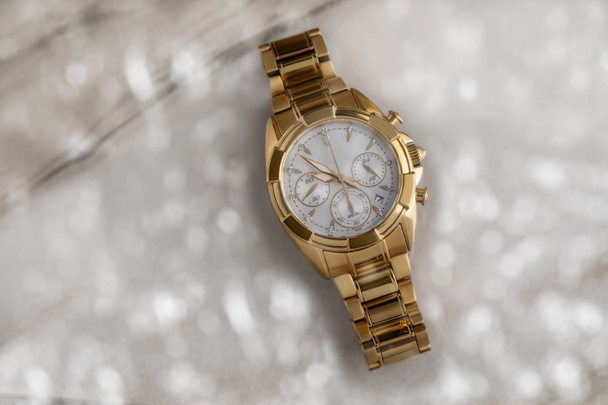 cher belle montre dames en or avec un bracelet en métal et un chronomètre sur un fond de marbre avec bokeh dans des couleurs claires. Accessoire de mode femme. Concept de vie riche, cadeau de vacances, vue sur le dessus - Photo, image