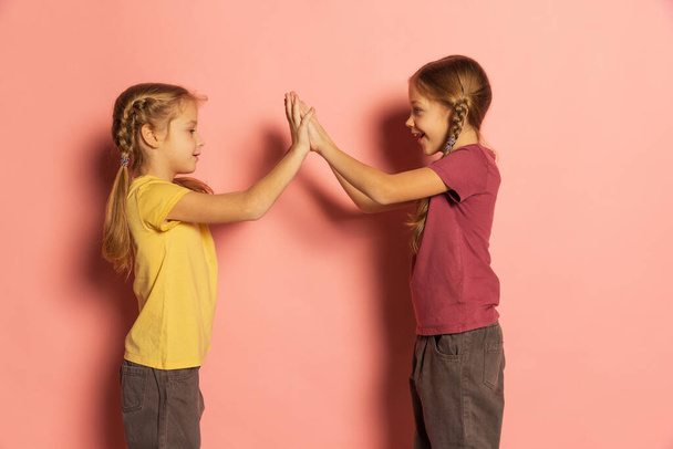 Cheerful little girls, sisters or siblings wearing casual style clothes playing isolated on pink background. Concept of childhood, emotions - Photo, image