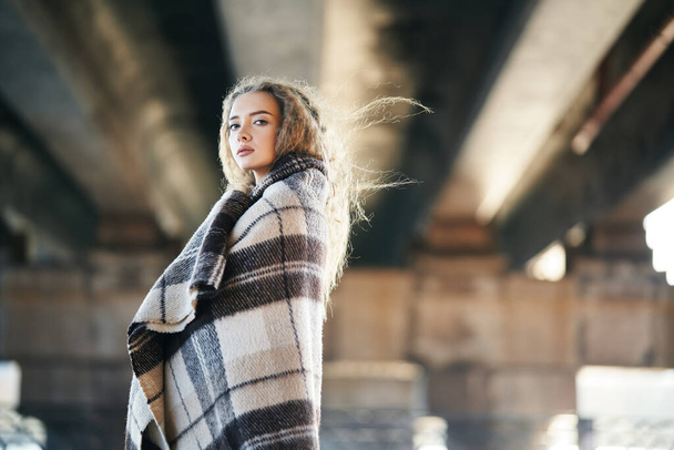 Portrait of pretty confident woman wrapped in wool blanket looking to camera posing on urban street background with copy space - Valokuva, kuva