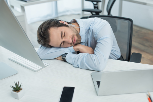 exhausted security man sleeping at workplace near laptop, monitor and smartphone with blank screen - Photo, Image