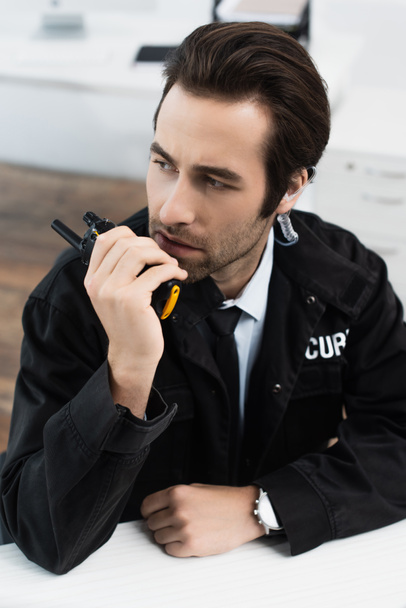 hombre de seguridad serio en uniforme negro llamando a walkie-talkie en la oficina - Foto, imagen