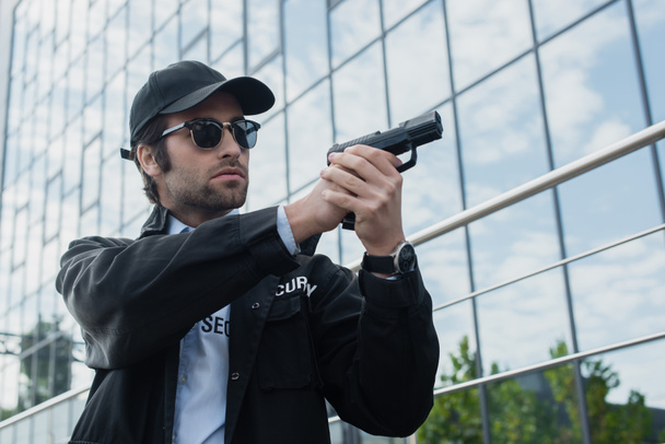 biztonsági őr fekete egyenruhában és napszemüvegben, fegyvert tartva, miközben a városi utcára néz. - Fotó, kép
