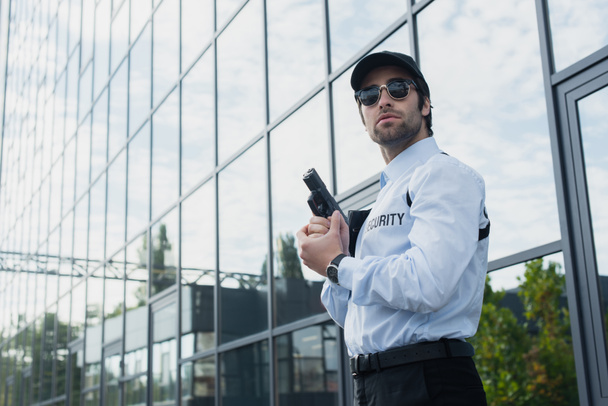 Güneş gözlüklü güvenlik elemanı cam cepheli bir binanın yanında duruyor. - Fotoğraf, Görsel