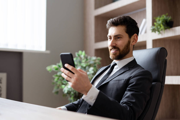 Businessman with elegant suit sitting at computer desk in the office - Adult man using app on mobile phone online, concepts about business and technology - Valokuva, kuva