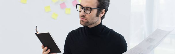 giovane uomo in occhiali e dolcevita nero che lavora con taccuino e documento, banner - Foto, immagini