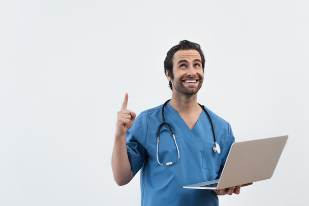 happy doctor with laptop looking up and pointing with finger isolated on grey - Foto, afbeelding