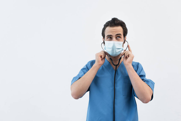 вдумчивый врач в медицинской маске, используя стетоскоп, изолированный на сером - Фото, изображение