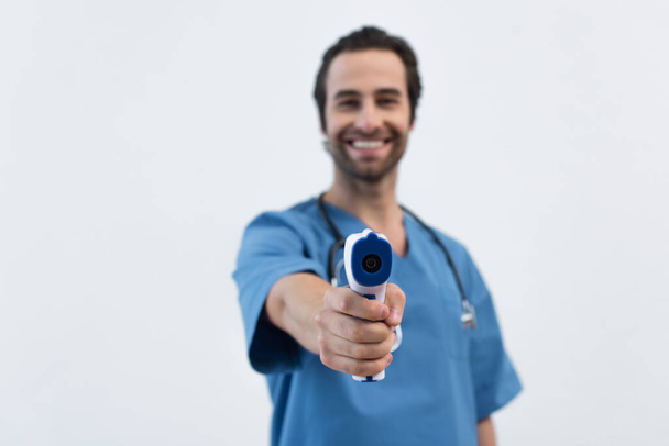 niewyraźny uśmiech lekarza trzymającego pirometr odizolowany na szaro - Zdjęcie, obraz