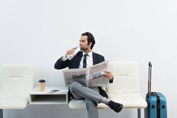Mann trinkt Wasser, während er mit Reisezeitung in der Abflughalle sitzt - Foto, Bild