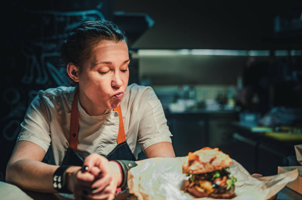 young woman chef with burger sitting in the kitchen in a cafe or restaurant - Photo, Image