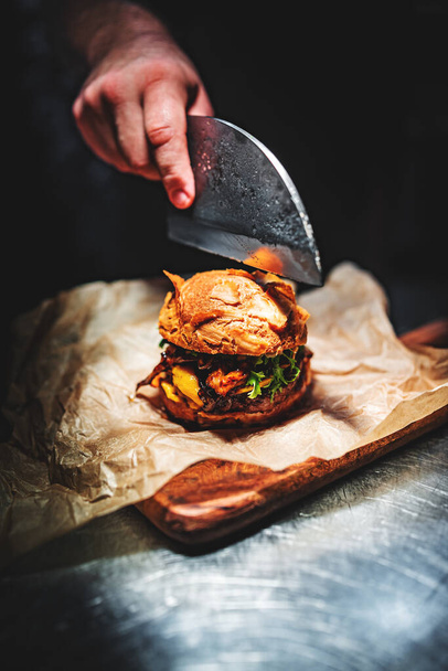 chef hand cuts a burger with his knife - Фото, зображення