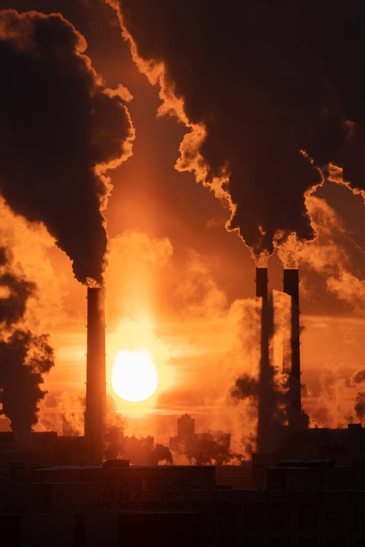 Угольная электростанция с дымящимися трубами на фоне красного заката. Загрязнение воздуха в зимнем городе - Фото, изображение