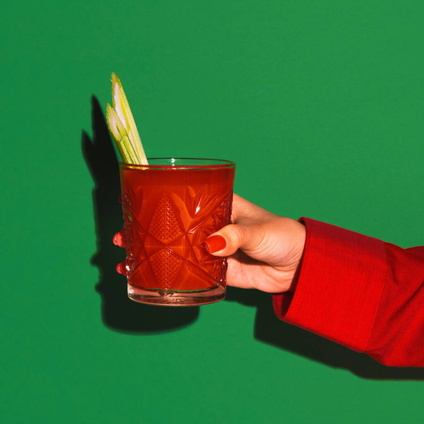 Female hand holding glass with cocktail bloody mary isolated on bright green neon background. Concept of taste, alcoholic drinks - Zdjęcie, obraz
