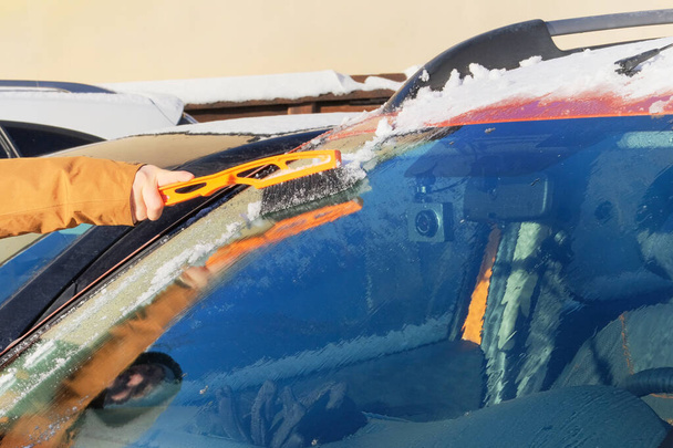 Человек очищает оранжевую машину от снега. Ветровое стекло машины. Кисть в руках мужчин. Зима, снег, транспорт. - Фото, изображение