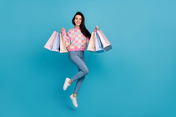 Photo of pretty shiny lady dressed print pullover jumping holding bargains empty space isolated blue color background - Photo, Image
