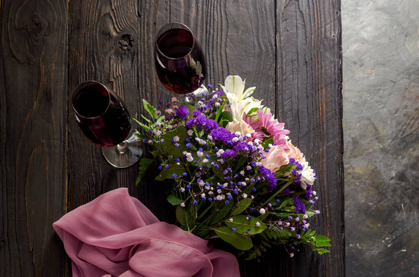Un ramo de flores diversas, suaves y festivas y dos copas de vino de cerca en una mesa de madera - Foto, Imagen