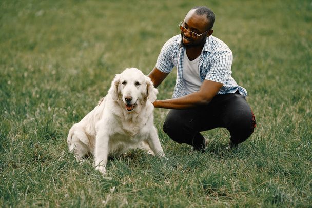 Black american man in a sunglasses sitting with has dog on a grass - Фото, изображение