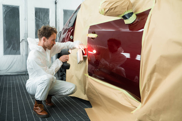 男性のカラーリストは、特別なランプを使用して車の塗料と色のサンプルを比較します。仕事中の自動車画家 - 写真・画像