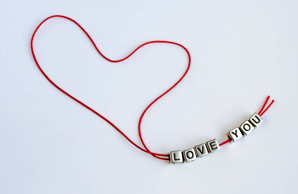Red thread in the form of a heart with square beads that make up the words LOVE YOU - Foto, afbeelding