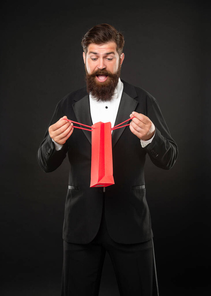surprised man in tuxedo bow tie formalwear on black background open shopping bag. valentines day - Фото, изображение