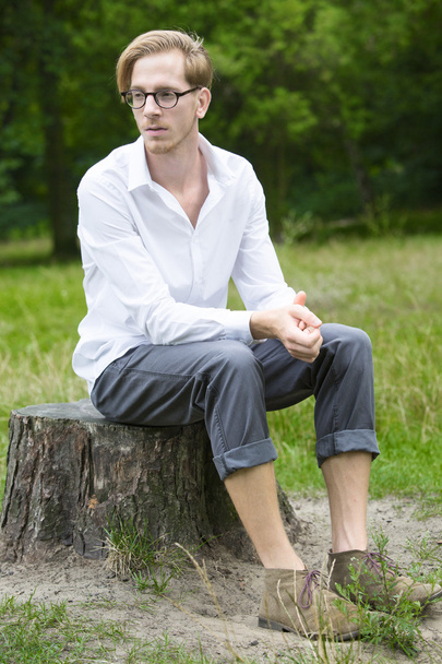 young man sitting on a tree stump - Foto, afbeelding