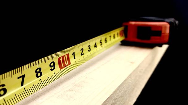 Uma barra de madeira feita de madeira de frutas é medida com uma fita métrica para trabalhos de construção, os centímetros na tela mostram o comprimento do pau - Foto, Imagem