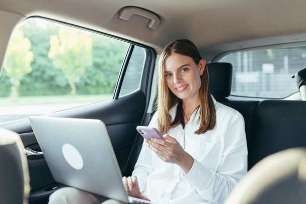 Beautiful female passenger car works on a laptop and uses a mobile phone - Photo, image