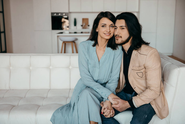 Um casal está sentado em um luxuoso sofá branco em seu novo apartamento - Foto, Imagem