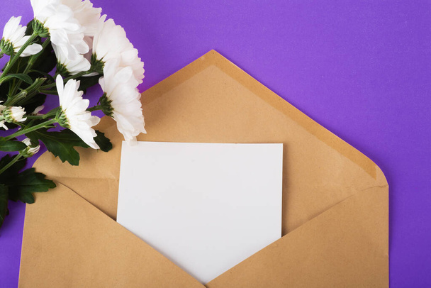 Opened craft paper envelope with empty piece of paper and white flowers near on very peri background. Zero waste concept. Organic material. Top view, copy space - Photo, Image