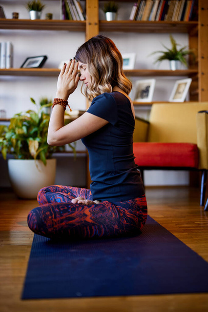 Duchowa kobieta joginowa siedząca w domu na macie do jogi w lotosowej pozie i modląca się. Yogi kobieta ćwiczy jogę w domu. - Zdjęcie, obraz