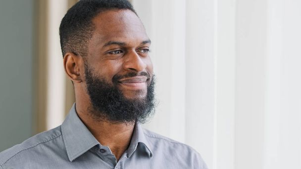 Smiling happy young African American guy, company employee holding glass getting drink of pure cold water. Healthy mixed race bearded man hydrating thirst, drinking at workplace, enjoying healthcare - Foto, Bild