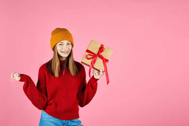 Young smiling happy hipster girl holding present boxes celebrating new year, wearing red knitted sweater and yellow hat. - Valokuva, kuva