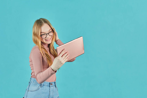 Smart looking girl with glasses. Social media and online communication. Attractive young student with digital tablet isolated on blue background. Studio shot - Photo, Image
