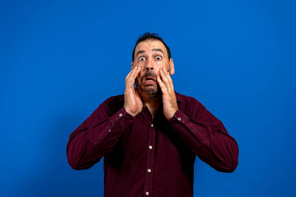 Young caucasian man isolated on blue background shocked, covering mouth with hands, anxious to discover something new. - Photo, Image