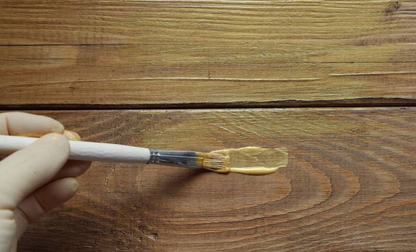 Рука використовує пензлик для нанесення золотої фарби на поверхню коричневого дерева
. - Фото, зображення