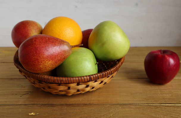 テーブルの上にはリンゴ、梨、オレンジのウィッカーボウルがあります。. - 写真・画像