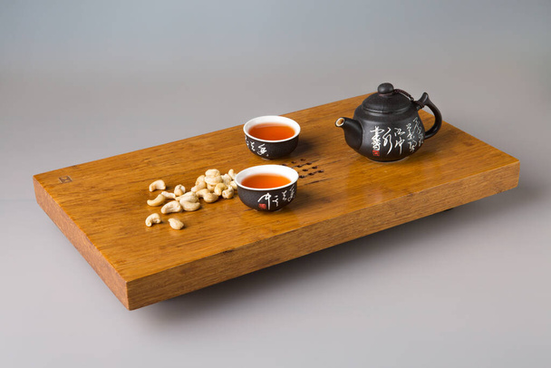 Kaksi perinteistä aasialaista teekuppia ja teekannu. Palvelu ja cashewpähkinöitä puinen pöytä teetä seremonioita. Minimalismin käsite. - Valokuva, kuva