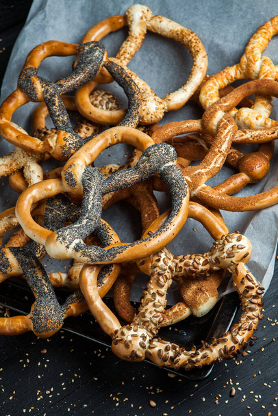 Fresh prepared homemade soft pretzels. Different types of baked pretzels with seeds on a black background. - Photo, Image
