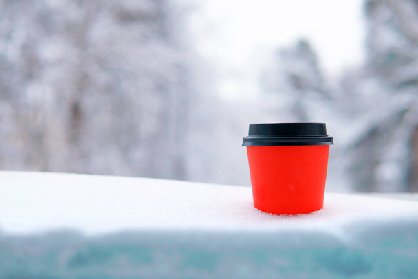 Red glass for coffee or tea in the snow in winter against the background of forest and nature. Copy space - Foto, Bild
