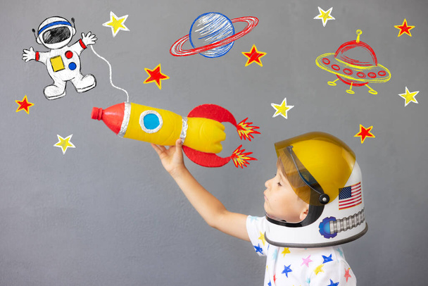 Happy child playing with toy rocket against concrete wall background. Kid pretend to be astronaut. Imagination and children dream concept - 写真・画像