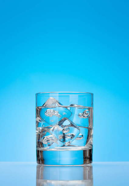Üveg vízzel és jégkockákkal a kék háttér felett - Fotó, kép