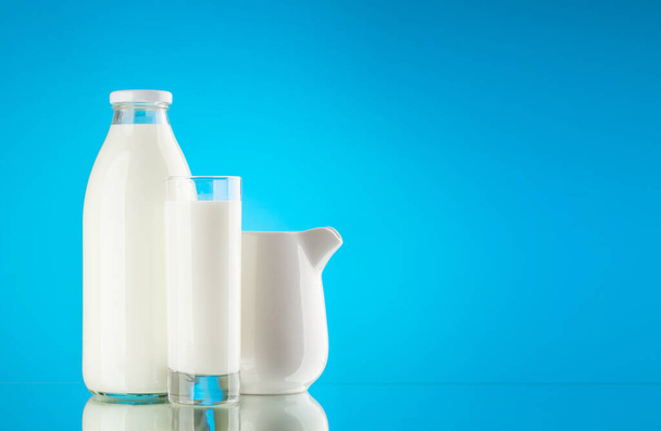 Μπουκαλάκι γάλακτος, γυάλινο και κανάτα σε μπλε φόντο με χώρο αντιγραφής. Γαλακτοκομικά - Φωτογραφία, εικόνα