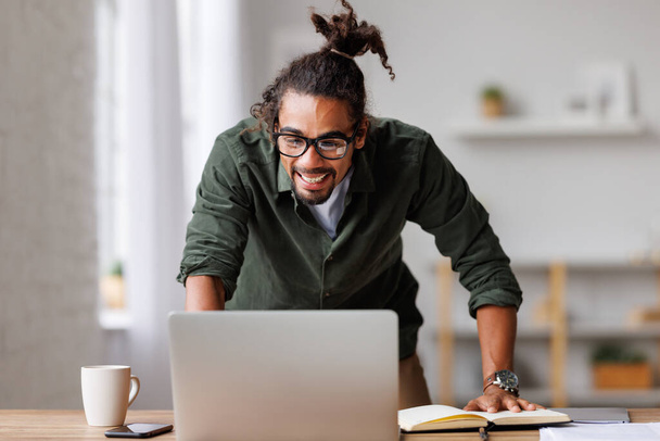 Задоволений афроамериканець, який дивиться на екран ноутбука, зрадіє, отримавши пропозицію. - Фото, зображення