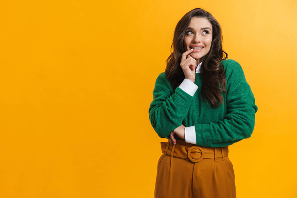 Young brunette woman in sweater smiling and looking aside isolated over yellow background - Foto, immagini