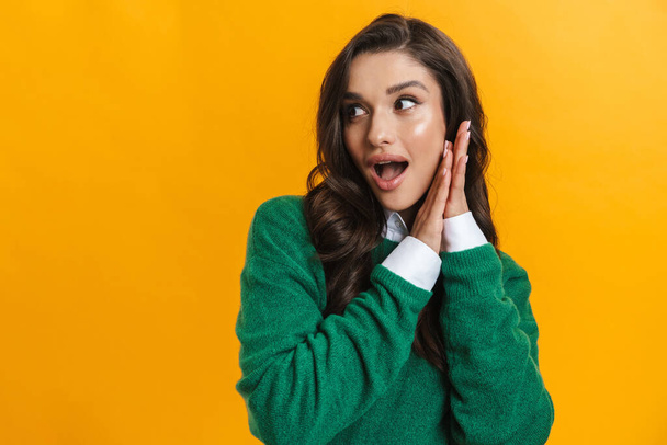Portrait of a young excited brunette woman standing isolated on a yellow background open mouth looking aside - Fotoğraf, Görsel