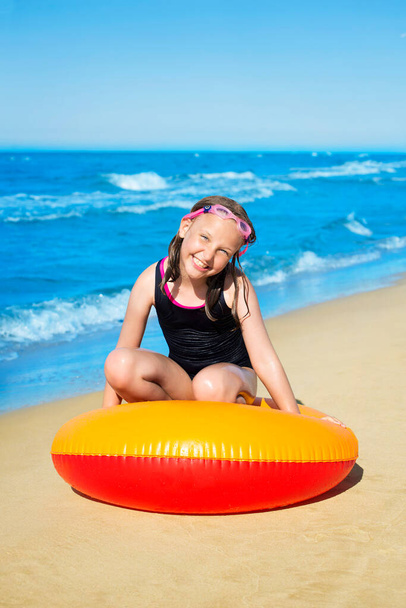 Jeune fille souriante assise dans un anneau de natation gonflable sur la plage de sable. Concept vacances d'été.  - Photo, image