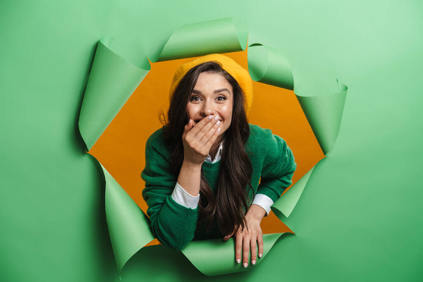 Молодая белая улыбающаяся женщина выглядывает из отверстия на зеленом фоне смеясь - Фото, изображение
