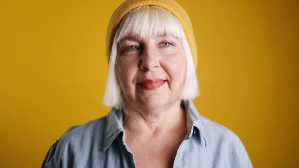 Krásná 50s žena s blond vlasy ve stylovém ležérní oblečení s copyspace při pohledu na kameru na žluté pozadí - Záběry, video