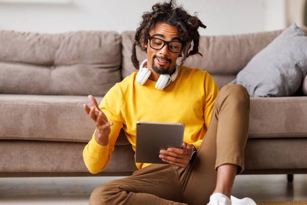 Dijital tabletli genç Afrikalı Amerikalı adam kendini izole ederken video aracılığıyla konuşuyor. - Fotoğraf, Görsel